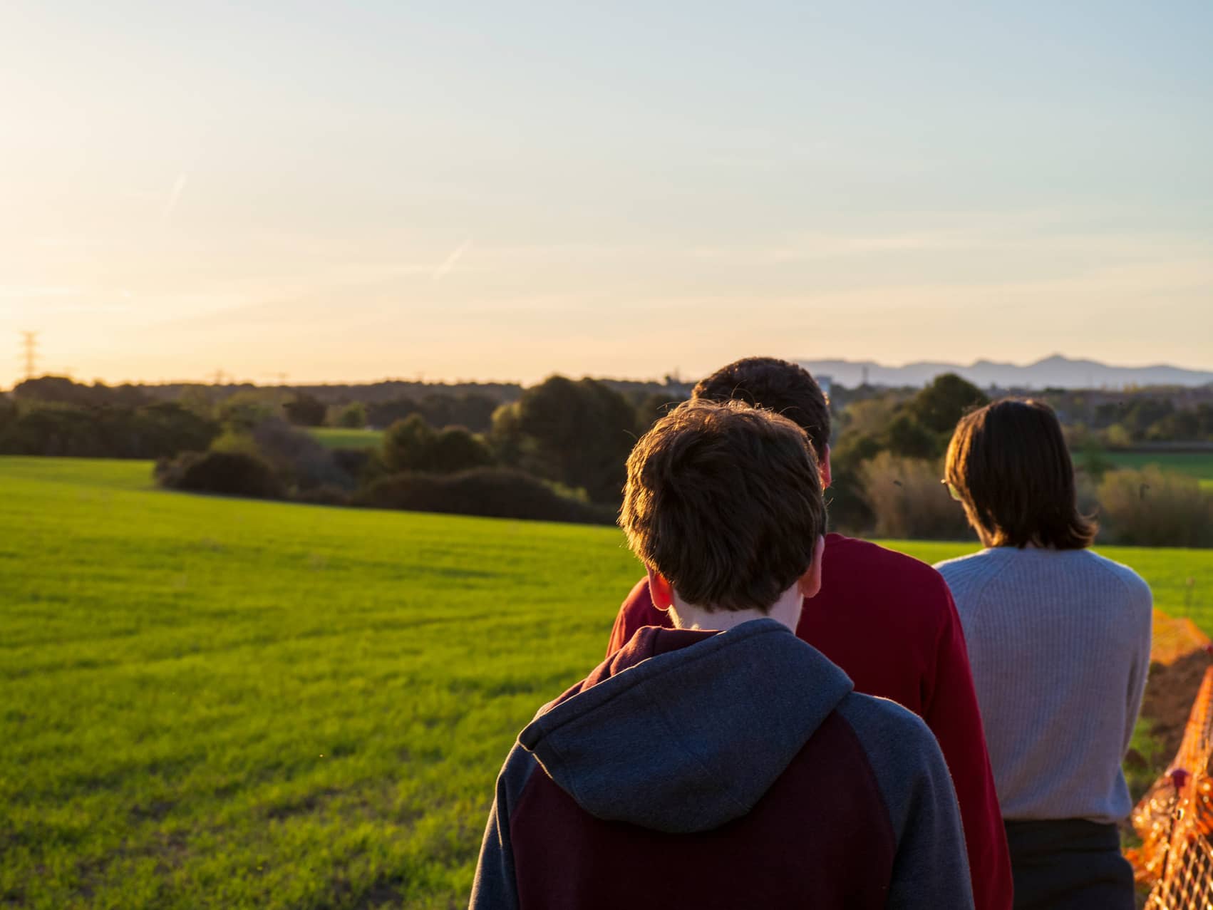 Trois personnes regardant ensemble un paysage verdoyant au coucher du soleil, symbole de l'horizon retraite et de la transmission familiale