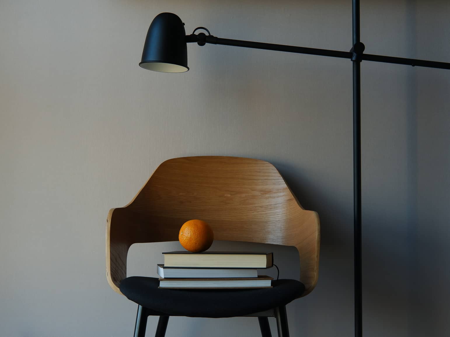 Nature morte minimaliste - fauteuil en bois, pile de livres de fiscalité et orange sous une lampe articulée, illustrant le calcul du Taux Marginal d'Imposition (TMI) pour la déduction PER